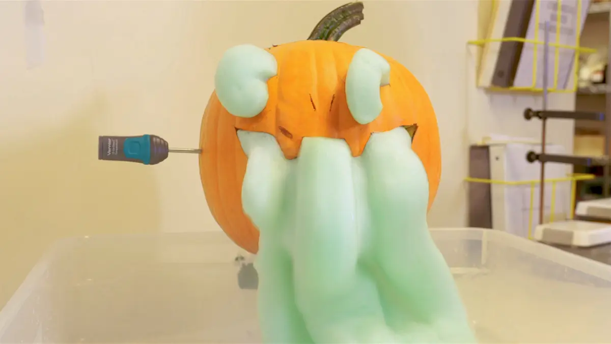 Calabaza tallada expulsando espuma verde por la boca y los ojos con una sonda de temperatura Vernier Go Direct insertada en su pared